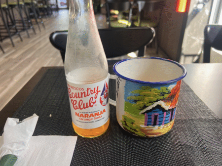 photo of orange beverage in a glass bottle next to a colorful mug