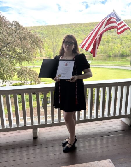 A woman standing on a porch showing her award.