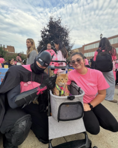 Batman and a woman crouch next to a dog in a stroller
